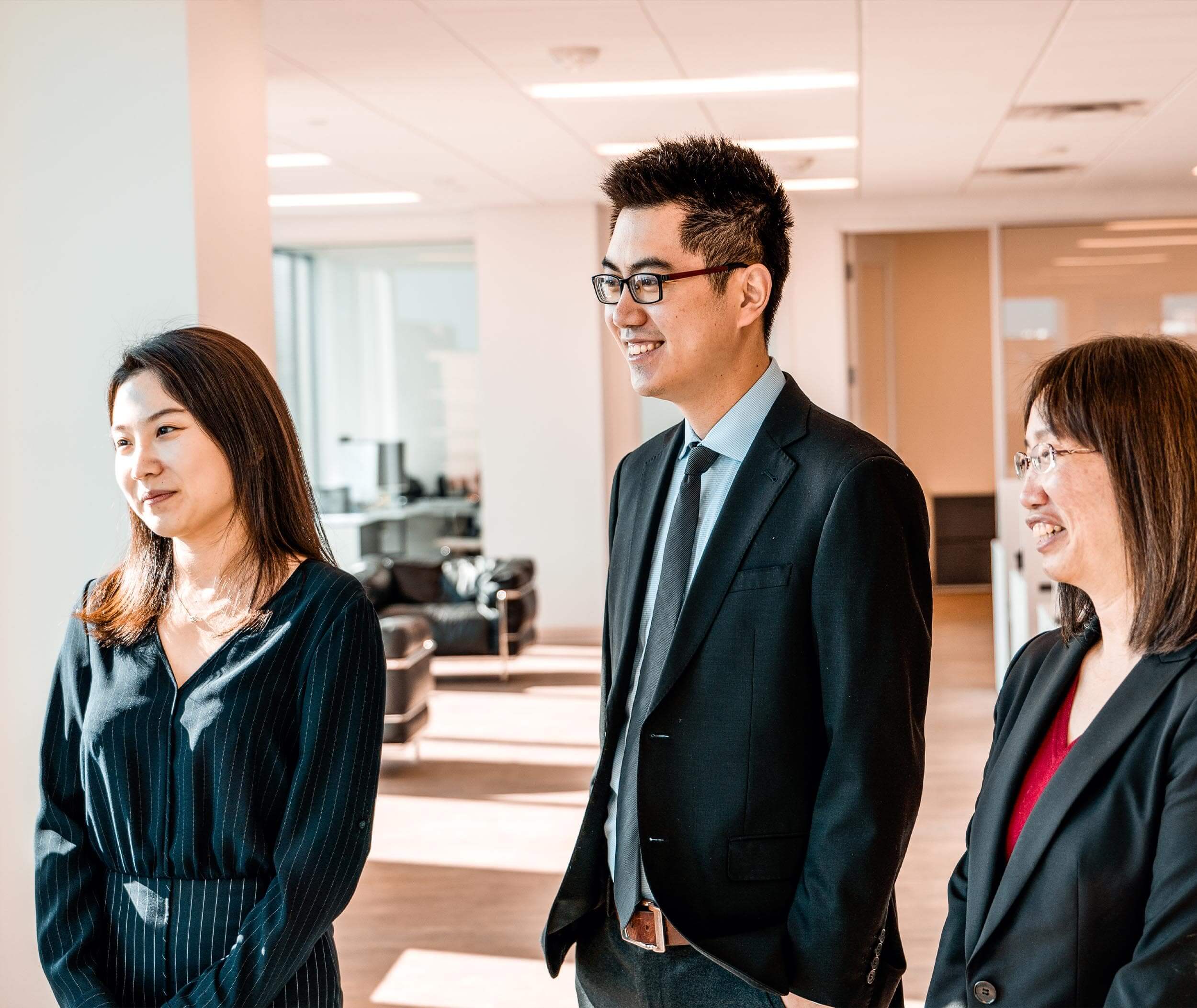 A photo of three SLCG Economic Consulting employees listening to someone speak and smiling.