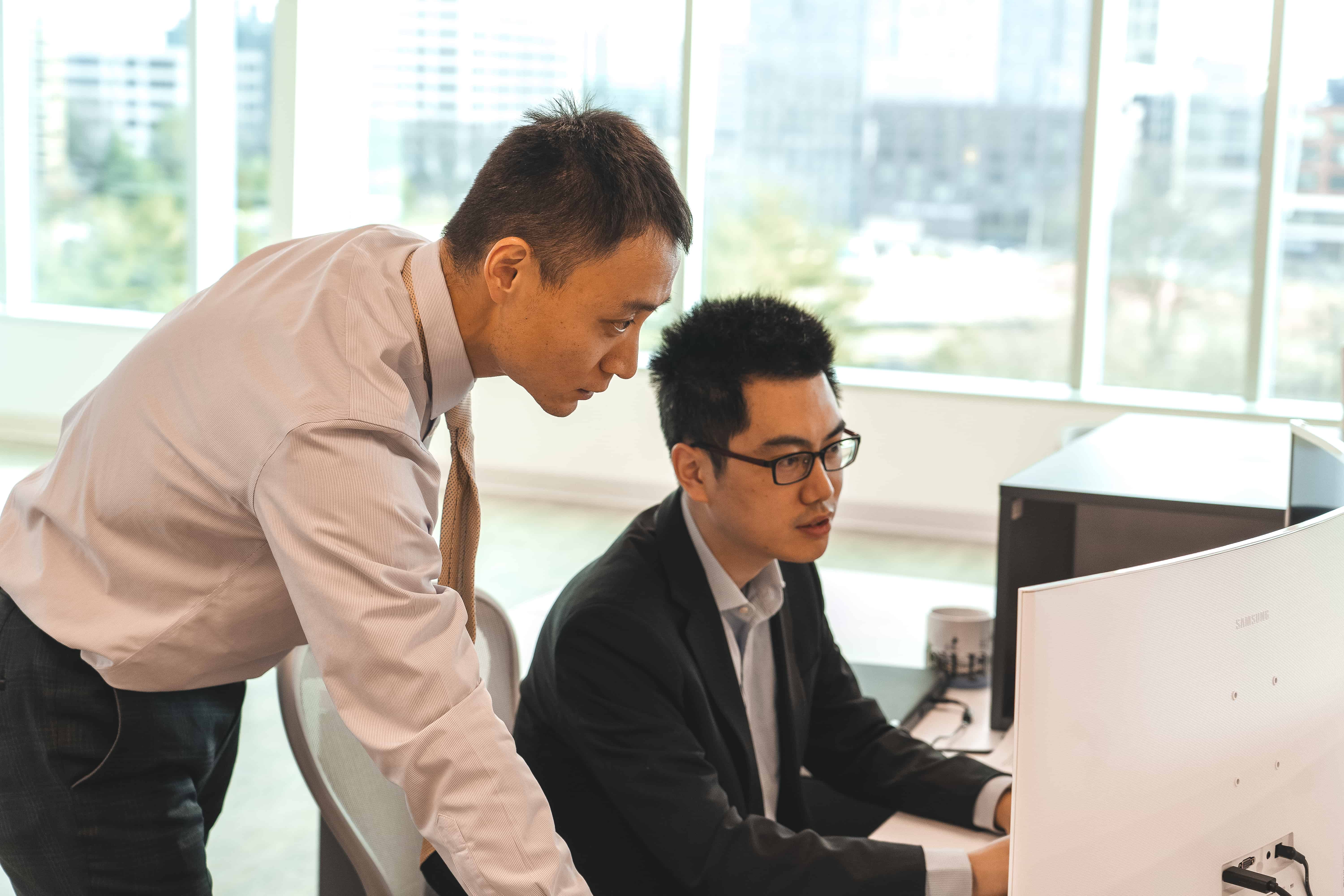 A photo of an SLCG Economic Consulting Principal giving feedback to an employee over his shoulder.